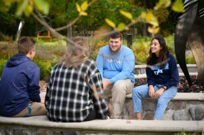 Students in 竞技宝app下载 gear sitting together in the woodsy campus